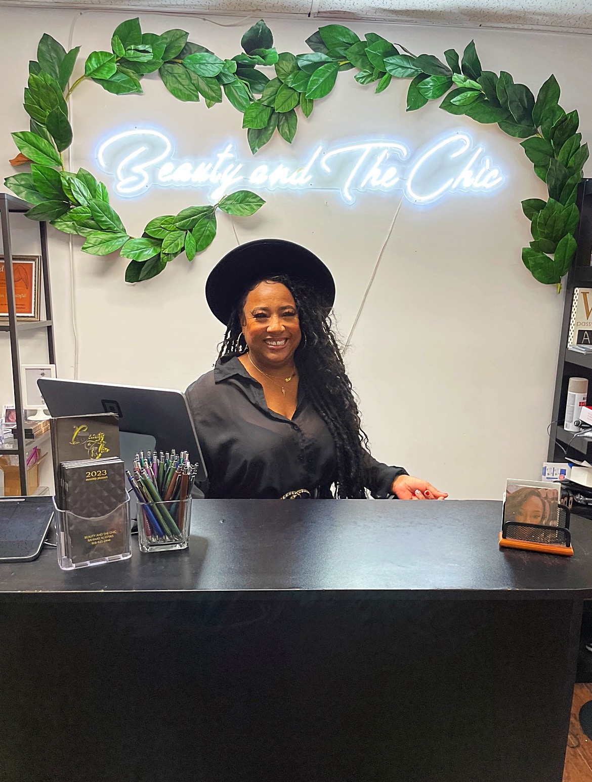 Front desk of Beauty and The Chic. Owner Chyreise Lambert stands behind the desk with a neon sign behind her that states the name of the business.