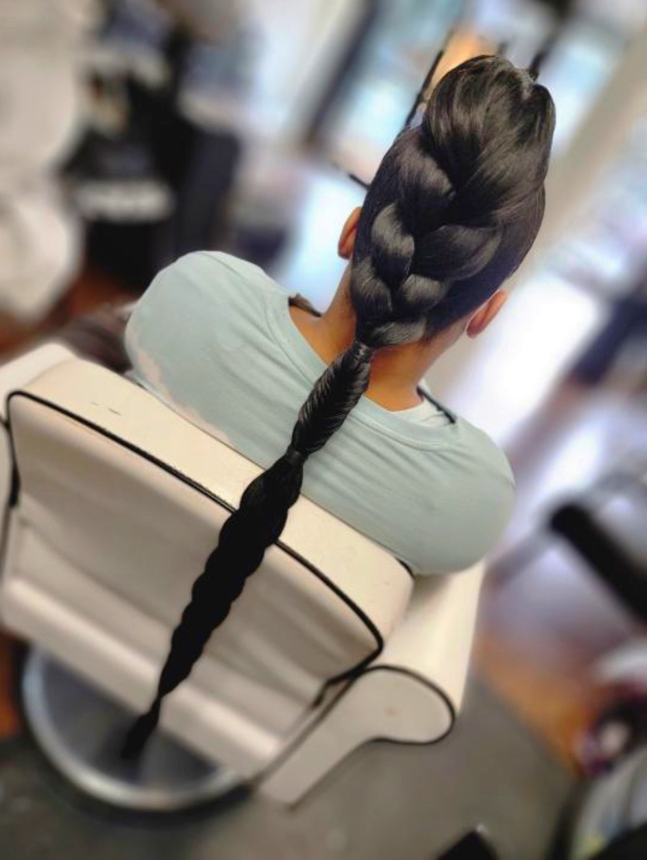 A woman with black hair that goes down her back, that has three distinct braid styles.